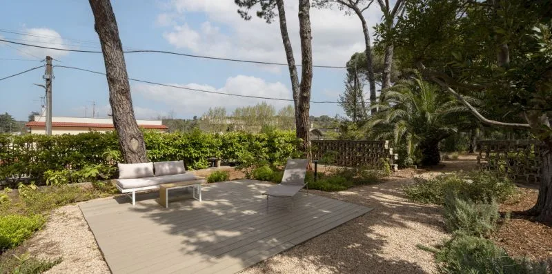 An outdoor patio with seating and a low hedge surrounded by trees.