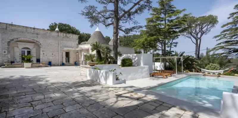 A stone courtyard with a swimming pool, white seating area, and surrounding trees.