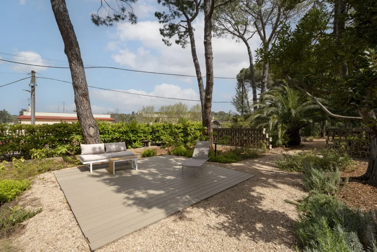 An outdoor seating area on a raised deck is surrounded by trees and shrubs.