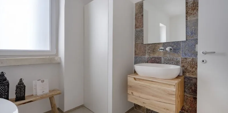 A bright bathroom with a white vessel sink above a wooden vanity.
