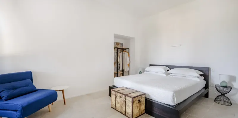A bedroom with a neatly made bed and a small seating area.