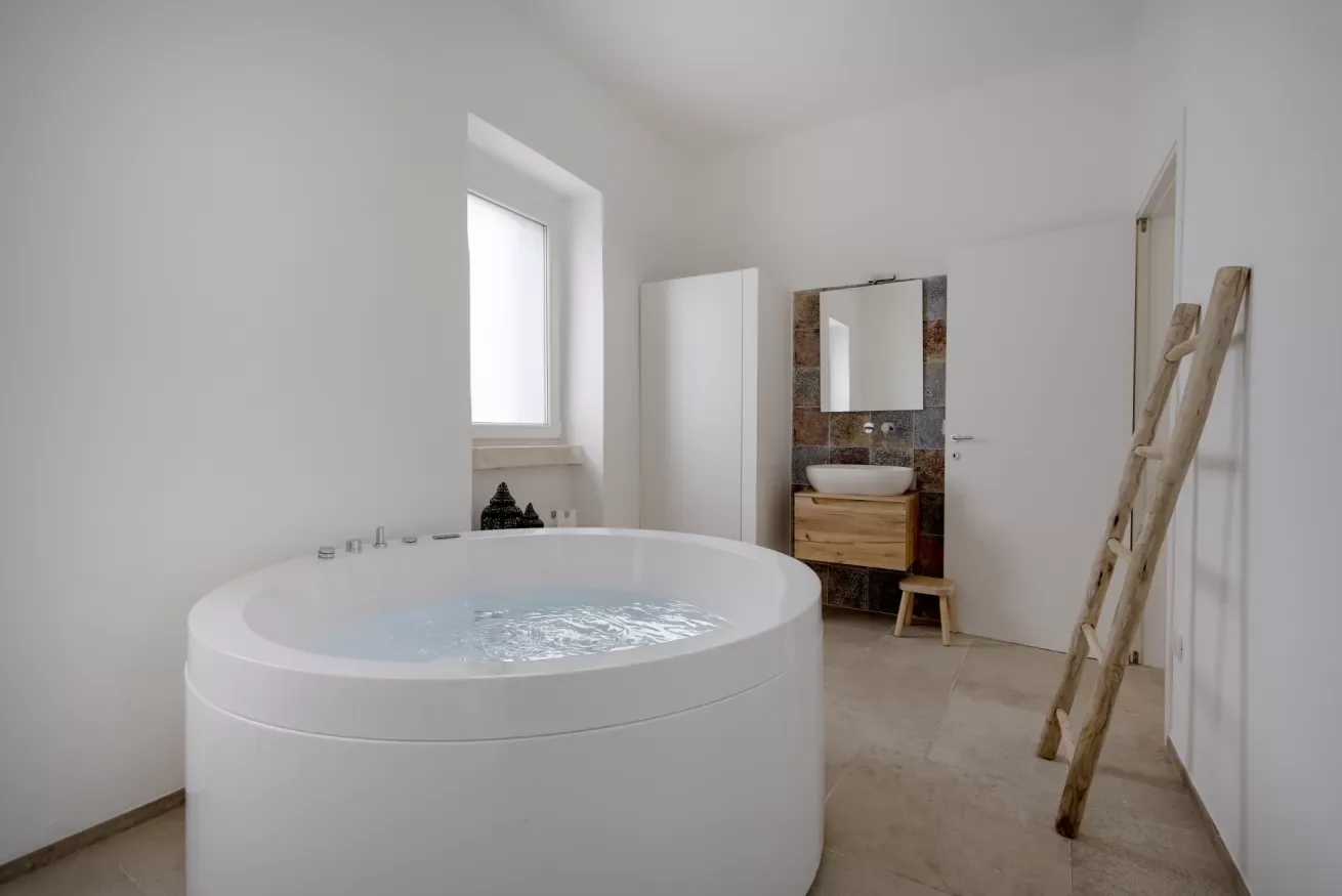A bright bathroom with a large round tub and a wall-mounted sink.