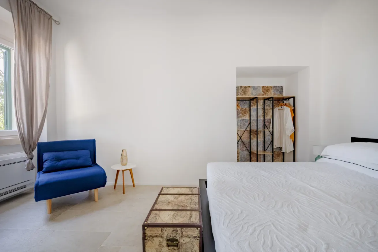 A bedroom with a bed, blue seating, and an open clothes rack.
