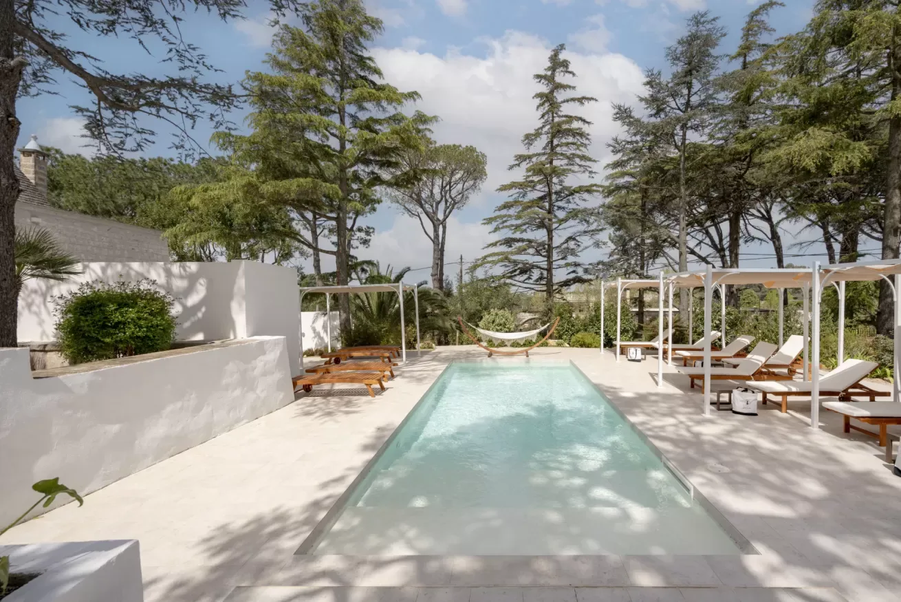 An outdoor swimming pool is surrounded by lounge chairs and tall trees.