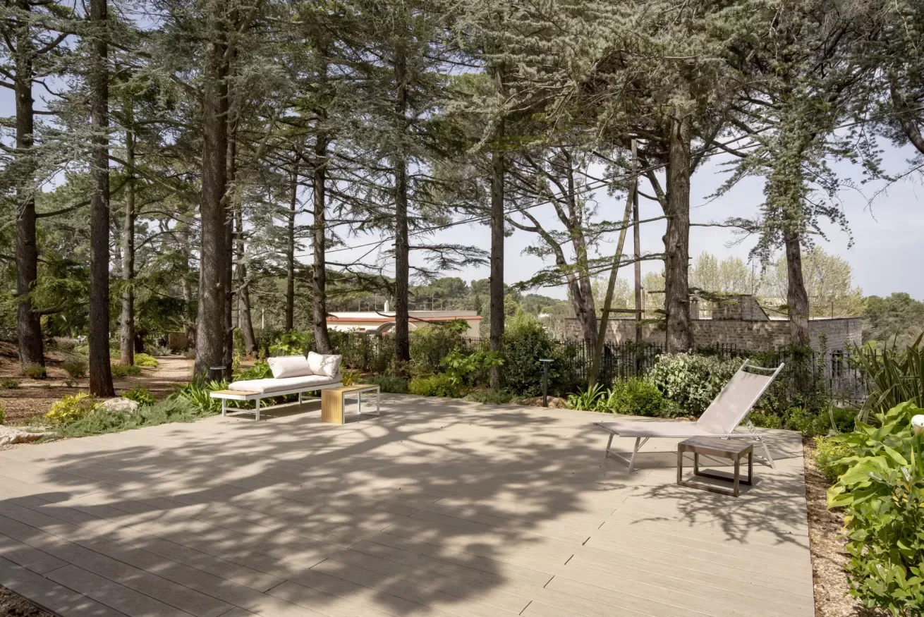 A paved outdoor terrace with lounge seating sits among mature trees and greenery.