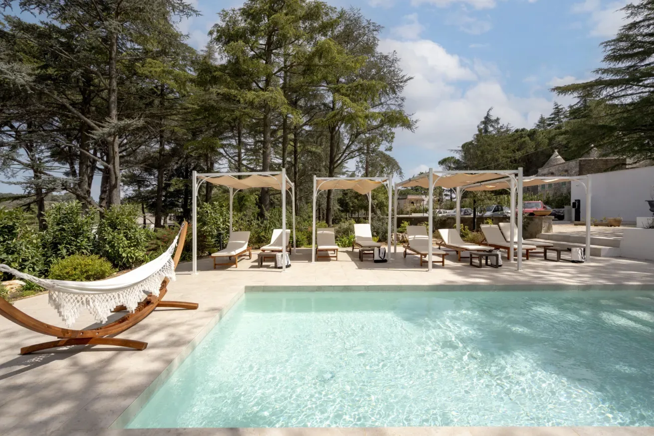 An outdoor swimming pool with lounge seating and a hammock among trees.