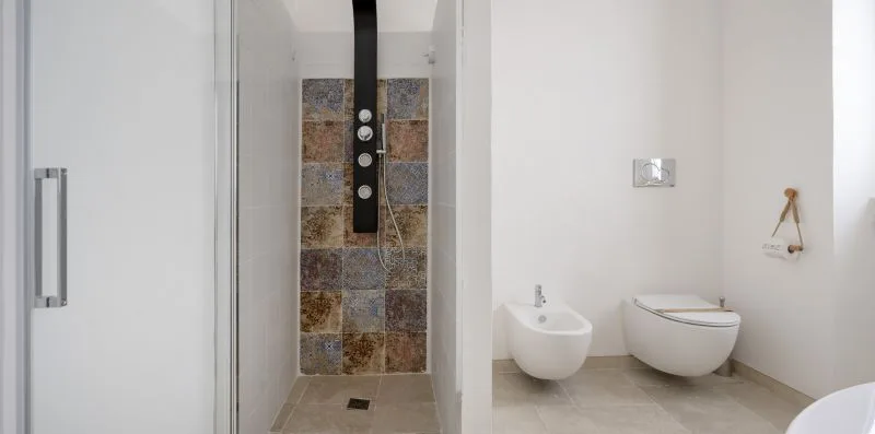 A modern bathroom with a tiled shower, wall-mounted sink, and toilet.