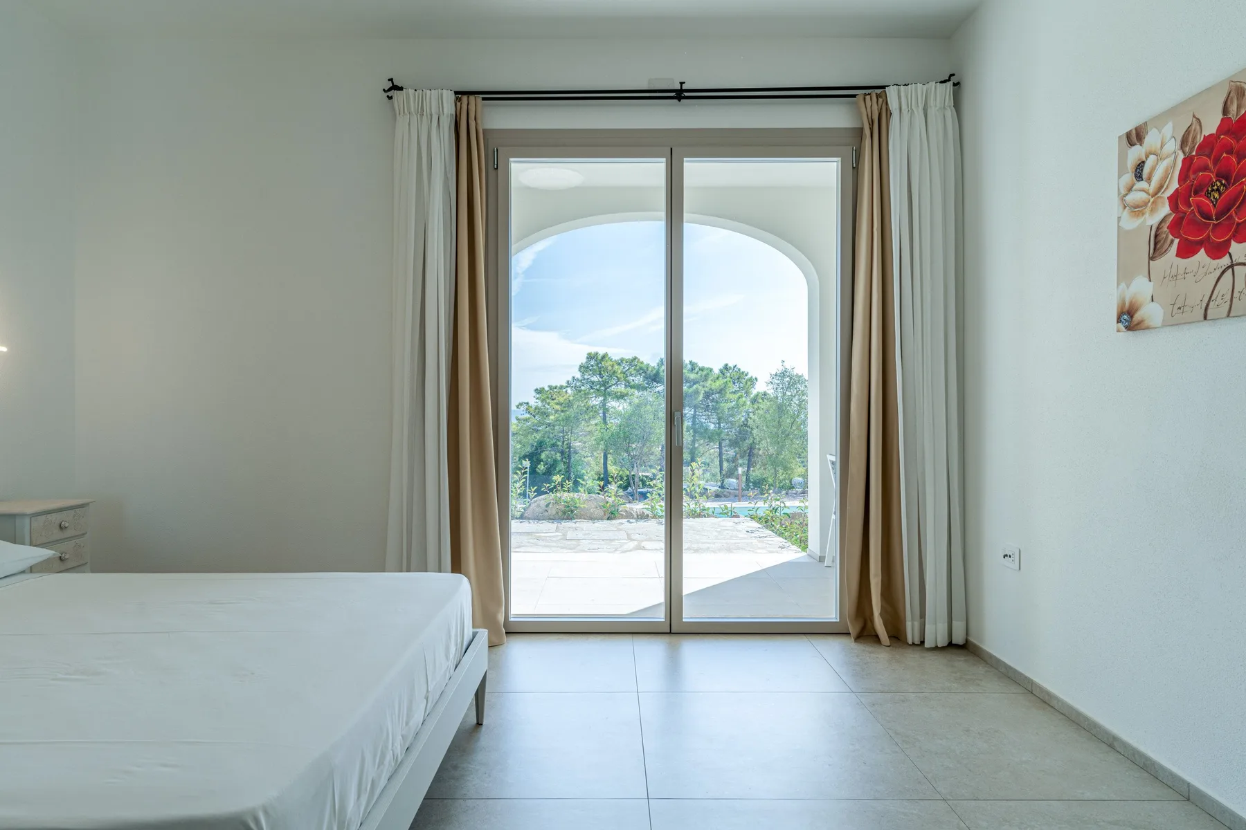 A bedroom with a bed beside glass doors opening onto a bright outdoor view.