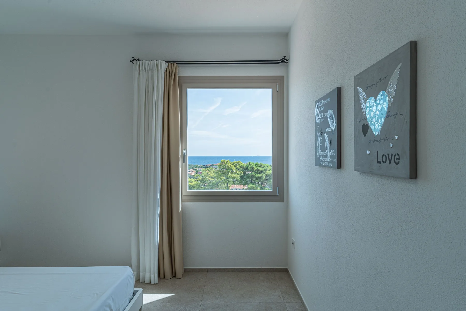 A bright bedroom with a bed, window, and ocean view.