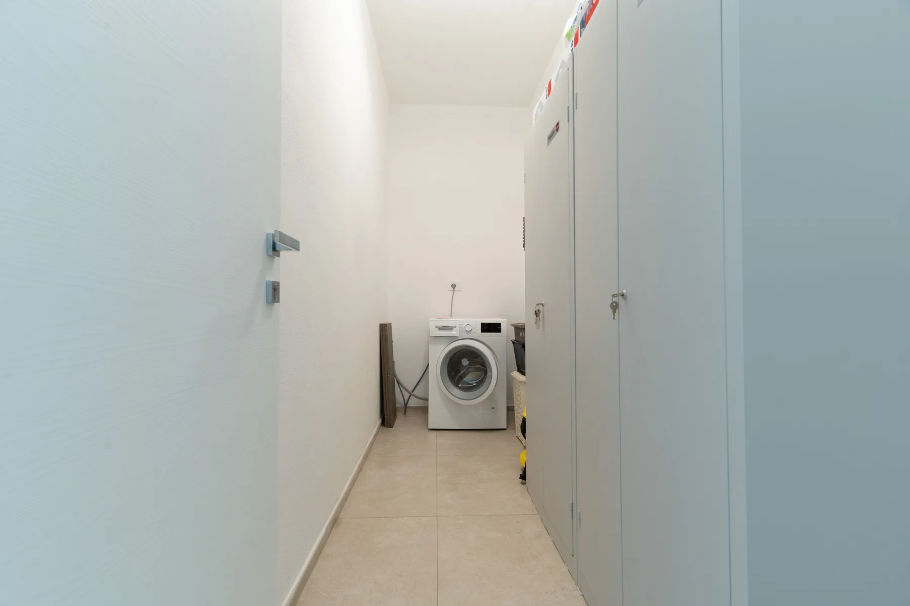 A narrow utility room with a washing machine and storage cabinets.