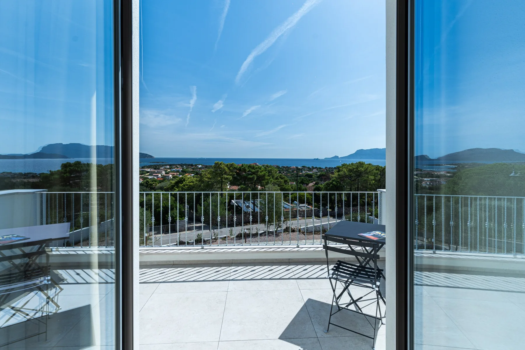 A balcony with seating overlooks a coastal town and the sea.