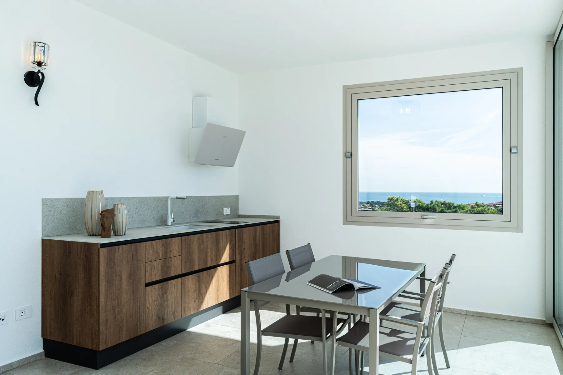 A bright dining area with a table and a wide window overlooking the sea.