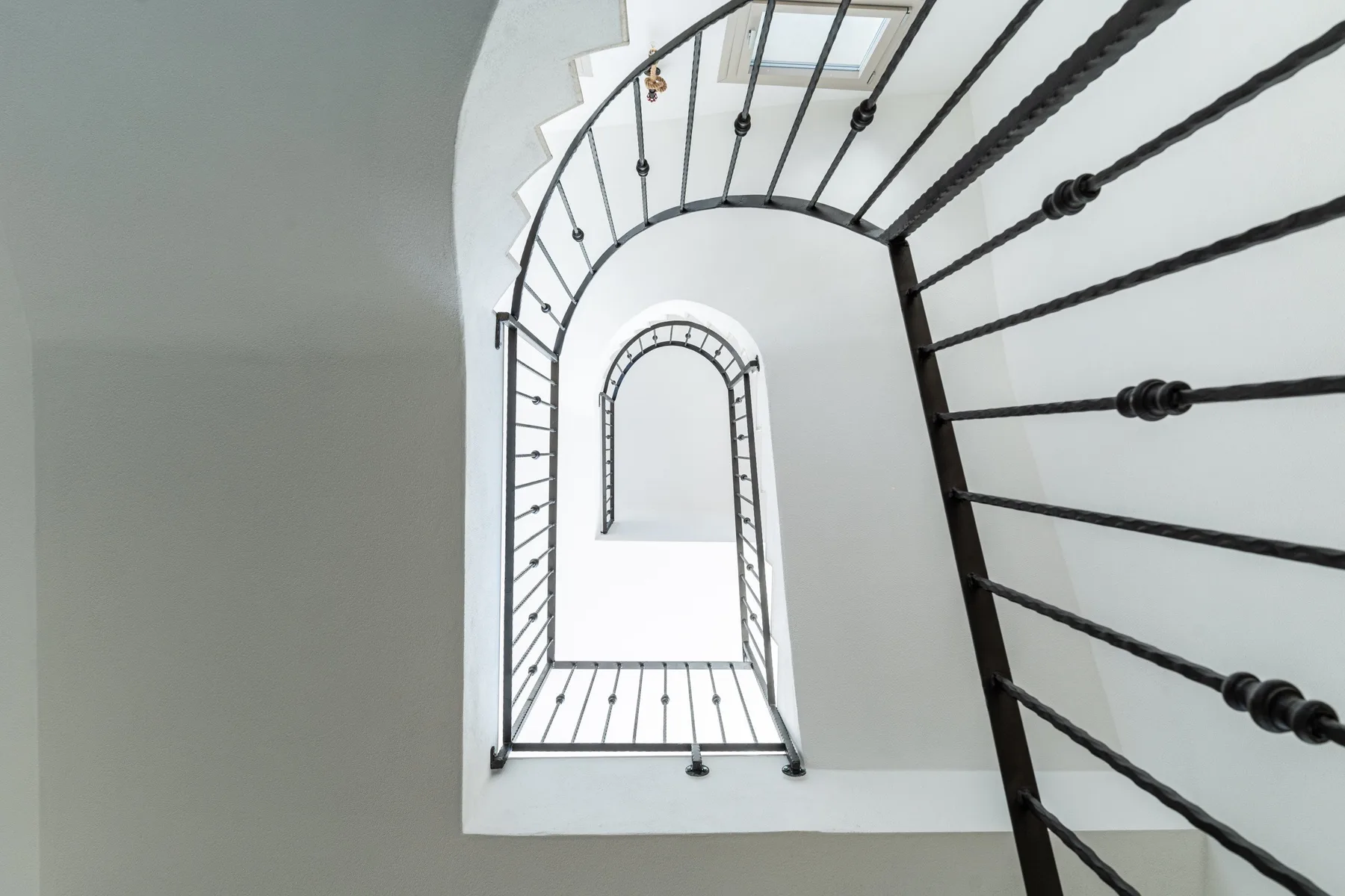 A view up a curved staircase with dark metal railings.