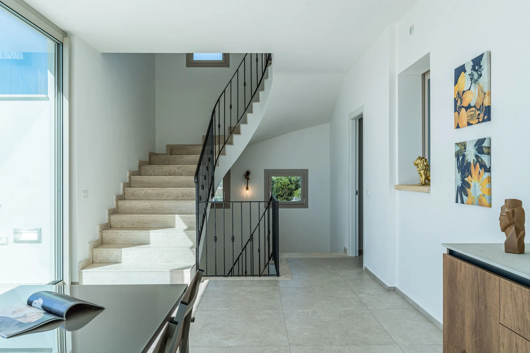 A bright interior hallway with a staircase and framed artwork.