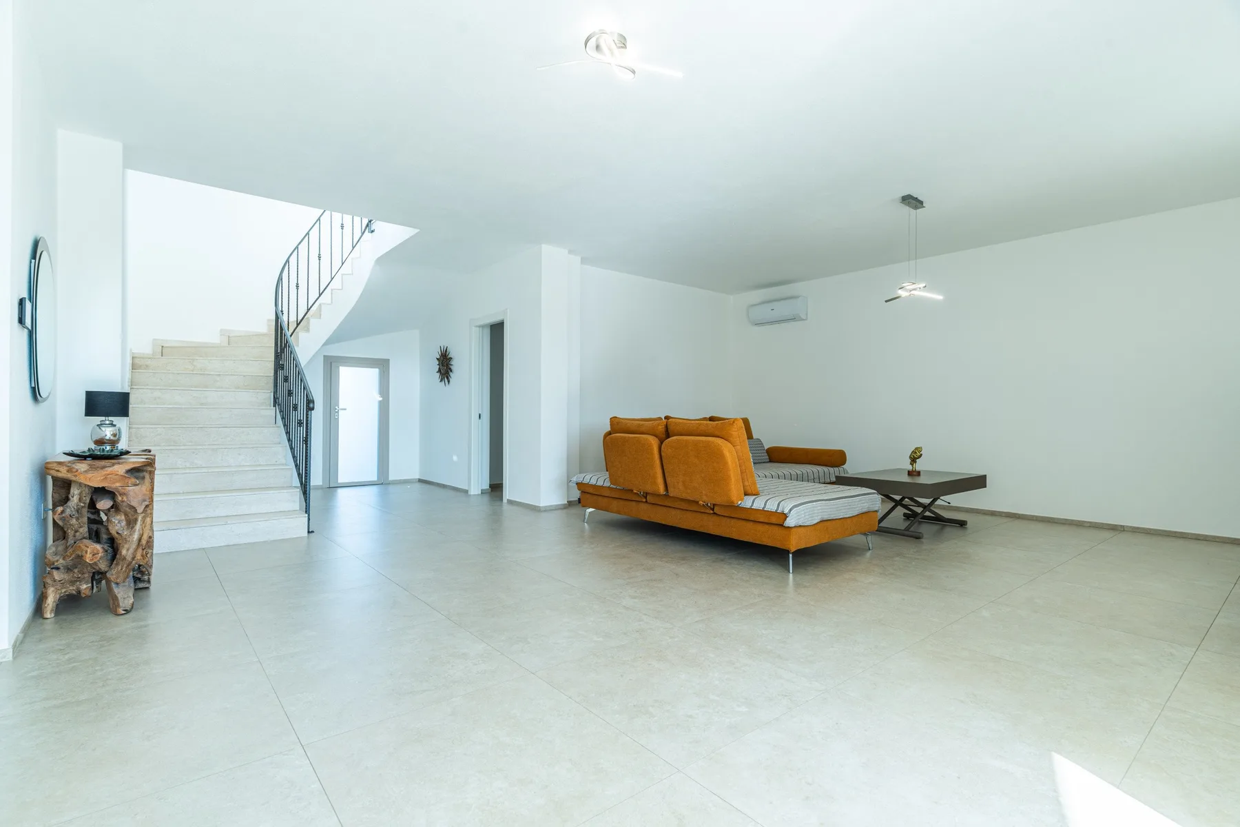 A bright open living area has orange seating beside a staircase.