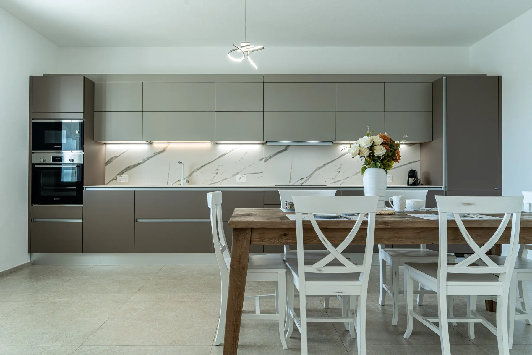 A modern kitchen and dining area with a long counter and white seating.