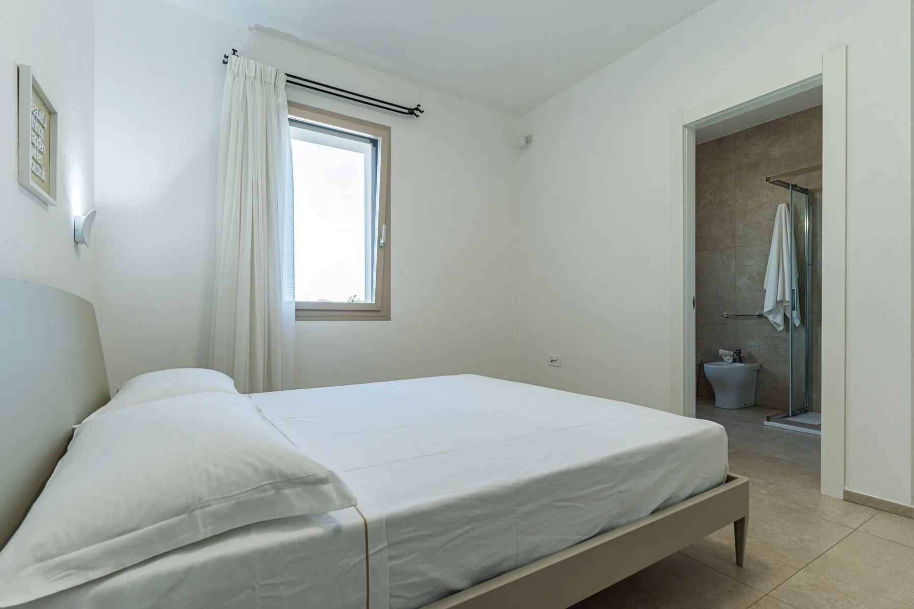 A bedroom with a bed beside a window and an open doorway to a bathroom.