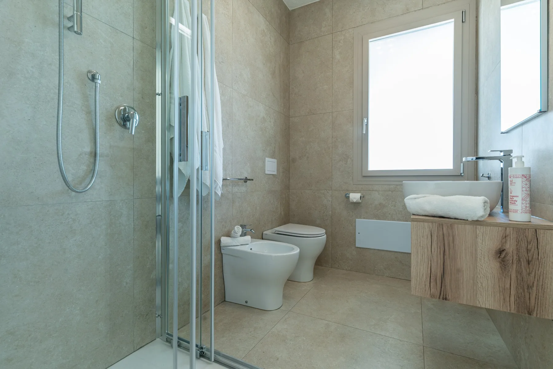 A tiled bathroom with a glass shower, toilet, bidet, and vanity.