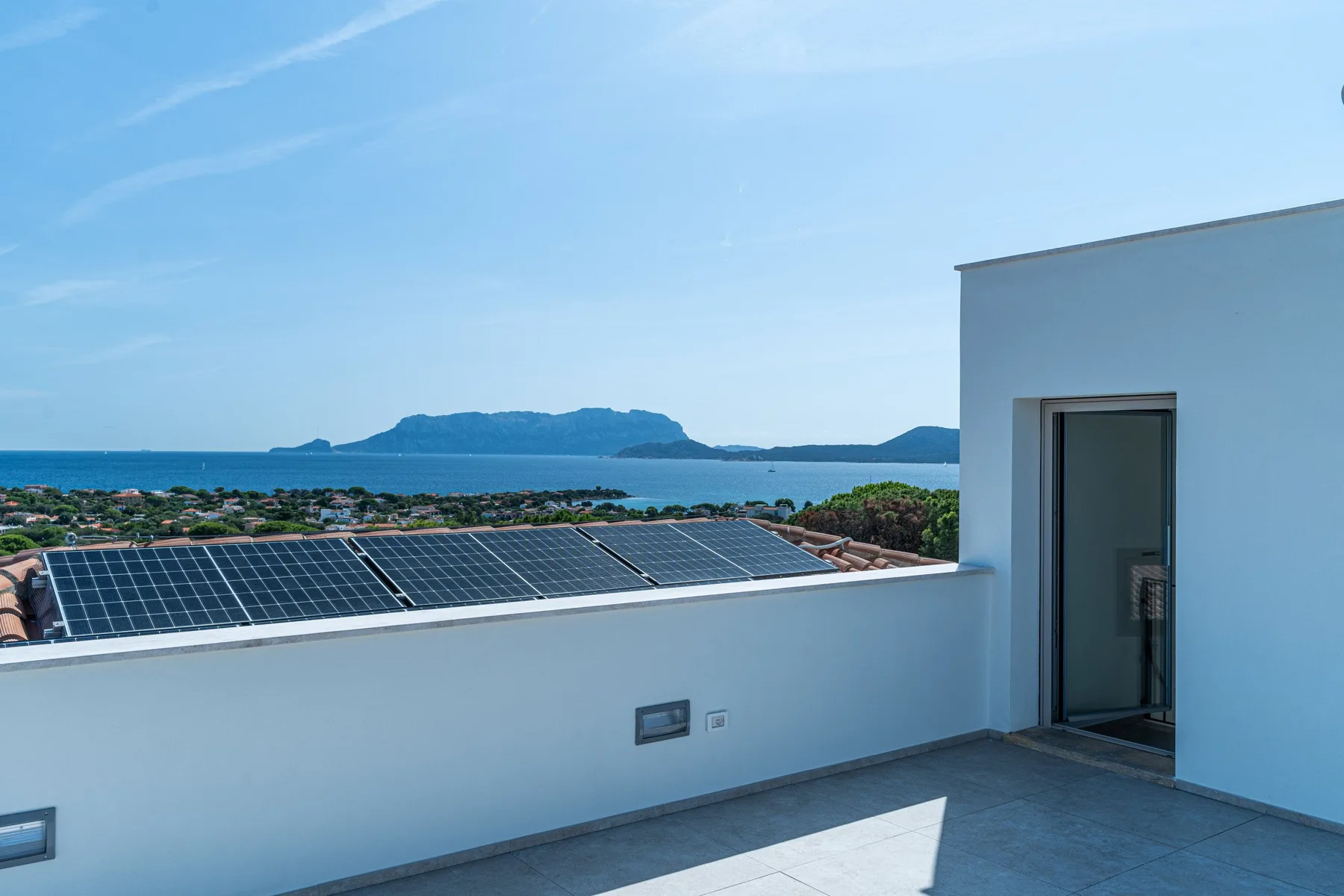 A rooftop terrace overlooks the sea, with solar panels visible beyond the parapet.