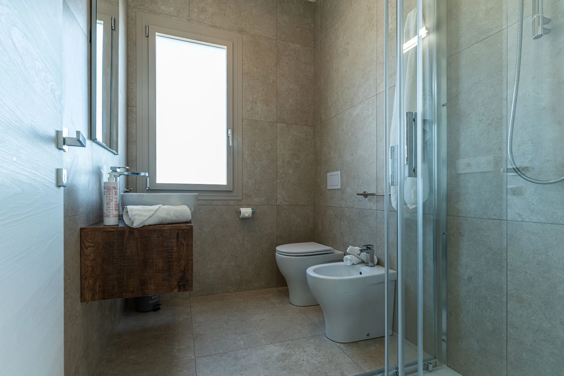 A tiled bathroom with a vanity, toilet, bidet, and glass shower.