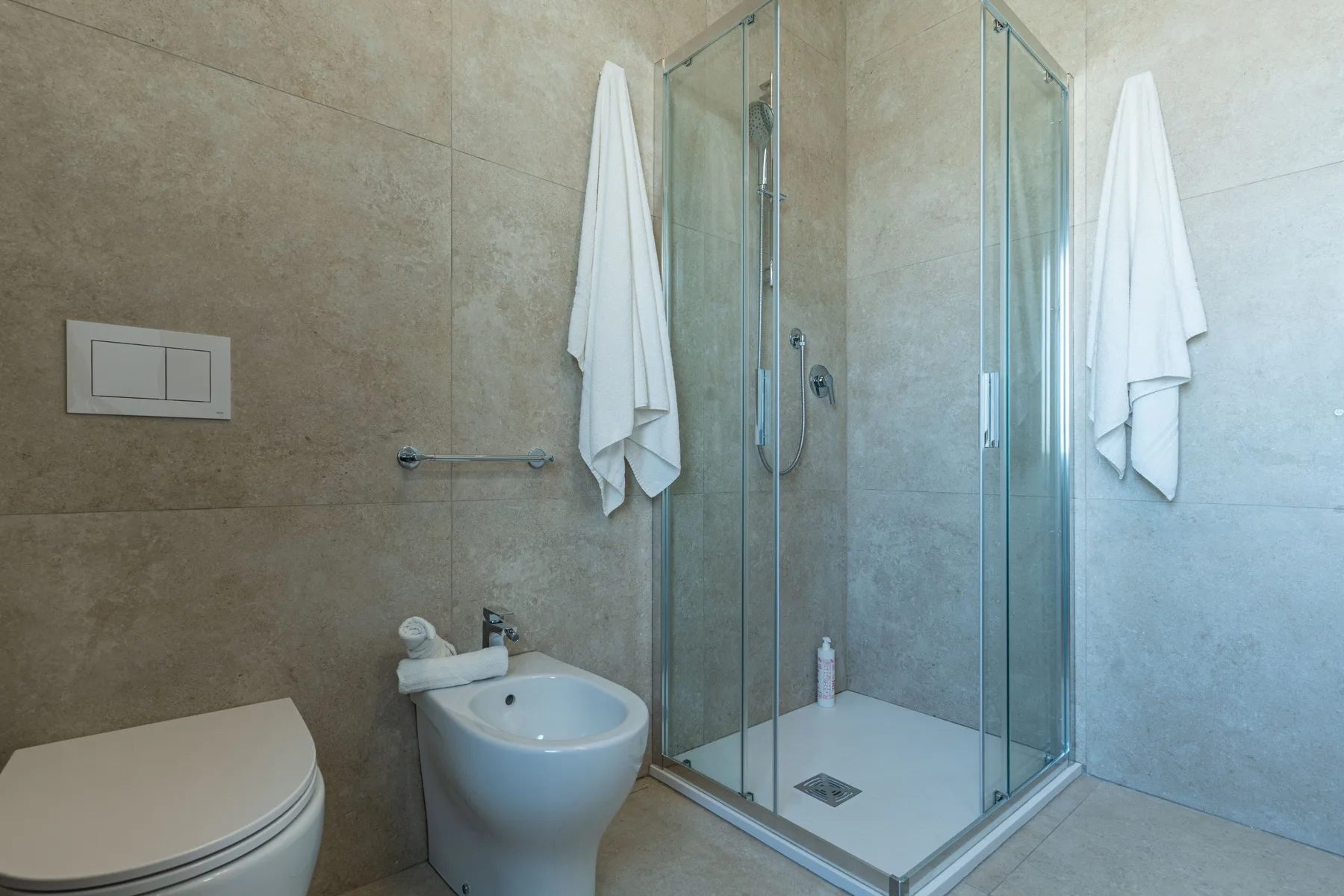 A tiled bathroom with a glass shower and white towels hanging nearby.
