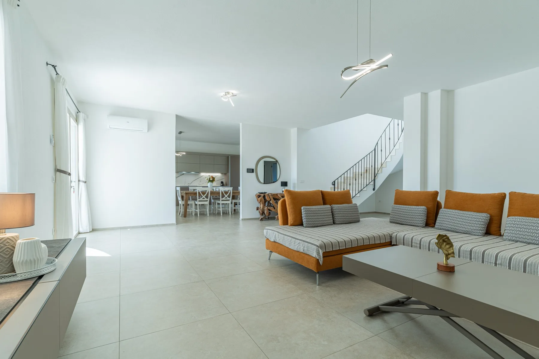 A bright open-plan living room with a dining area and staircase in the background.