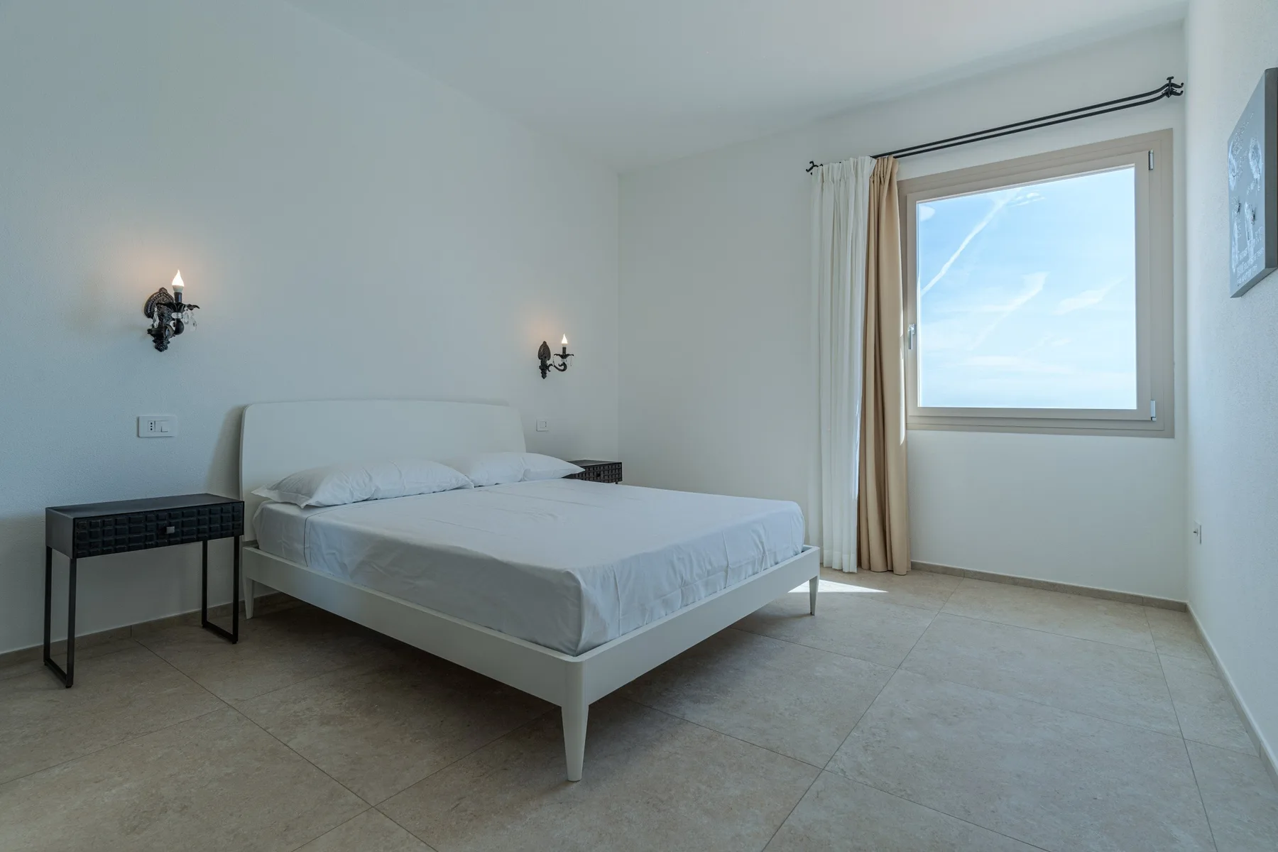 A bright bedroom with a neatly made bed and a large window.