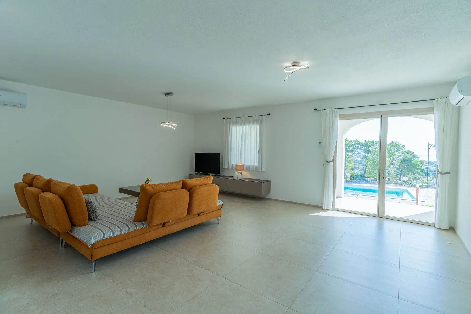 A bright living room with seating, a television, and sliding glass doors.
