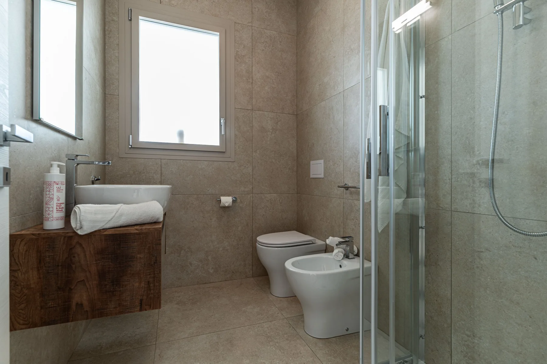 A tiled bathroom with a sink, toilet, bidet, and glass shower.