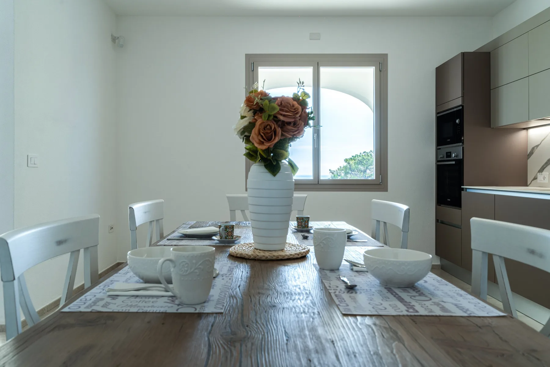 A dining area with a table set with dishes and a vase of flowers.