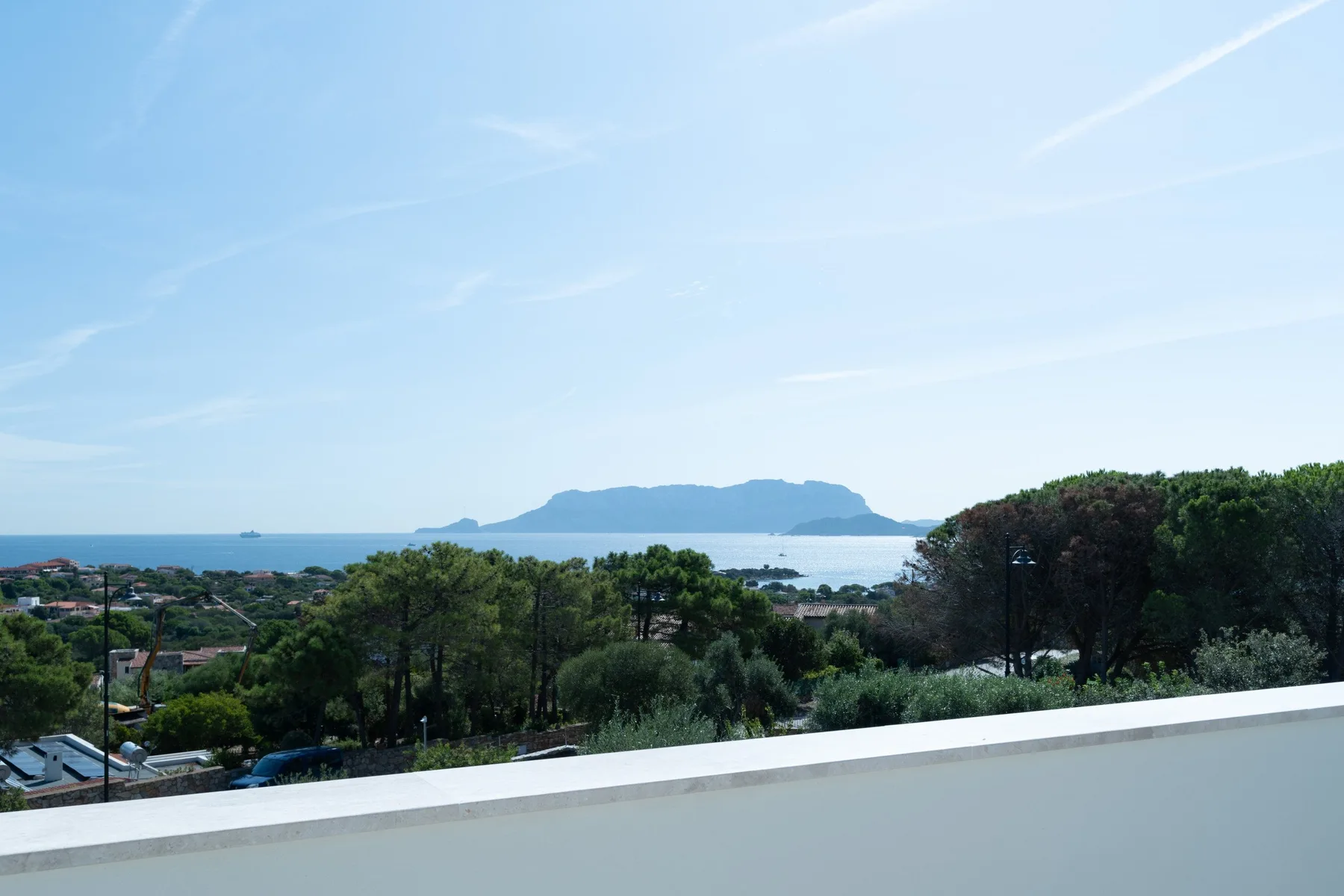 A sea view from a terrace overlooks greenery and a distant island.