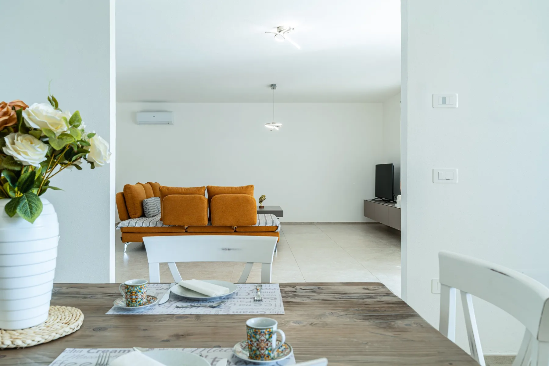 A bright living room with orange seating, a television, and a dining table in the foreground.