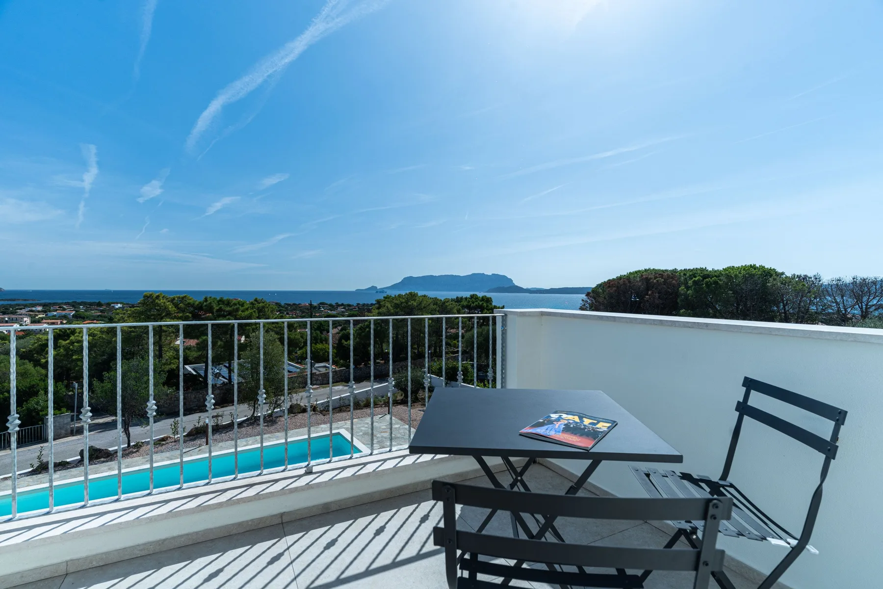 A terrace with outdoor seating overlooks the sea and a swimming pool.