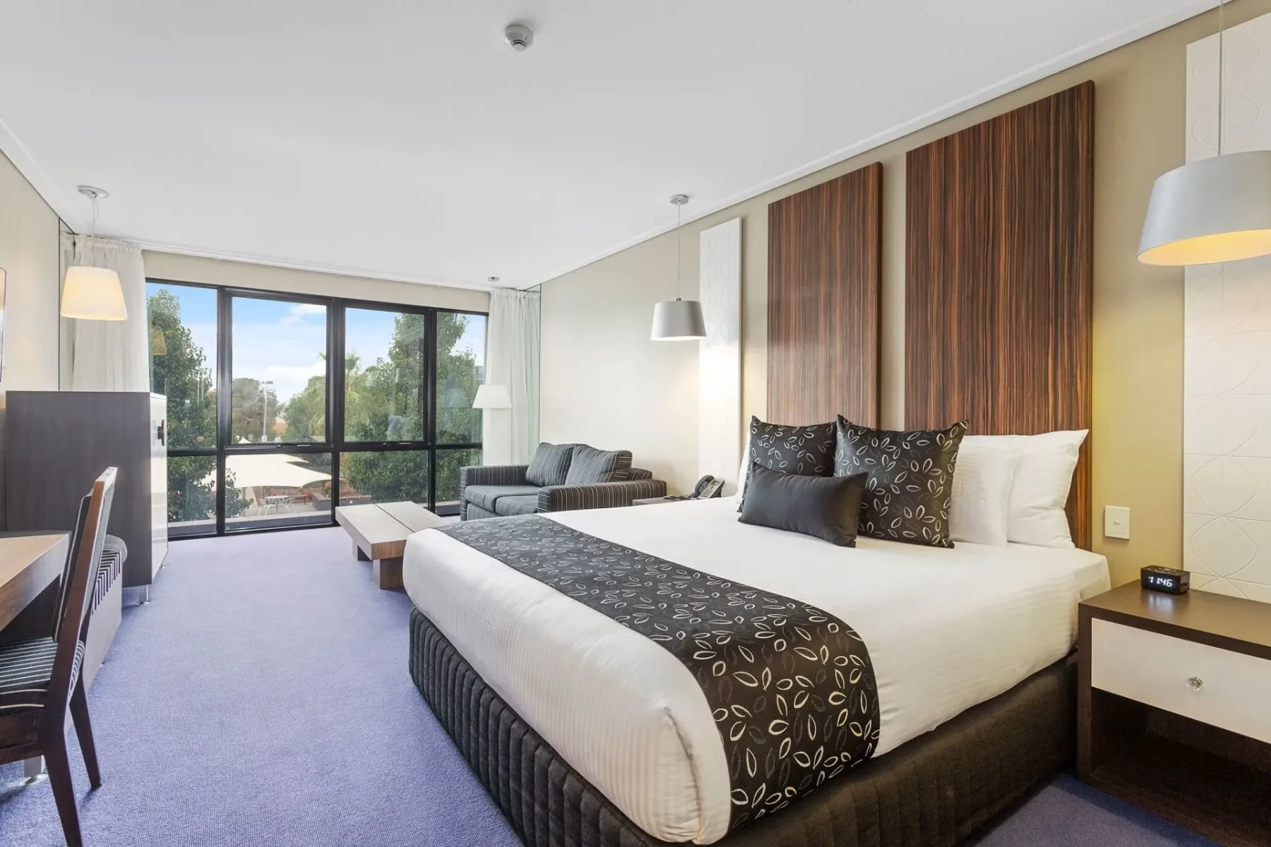 Dormitorio de hotel con una cama, sofá, escritorio y una ventana grande.