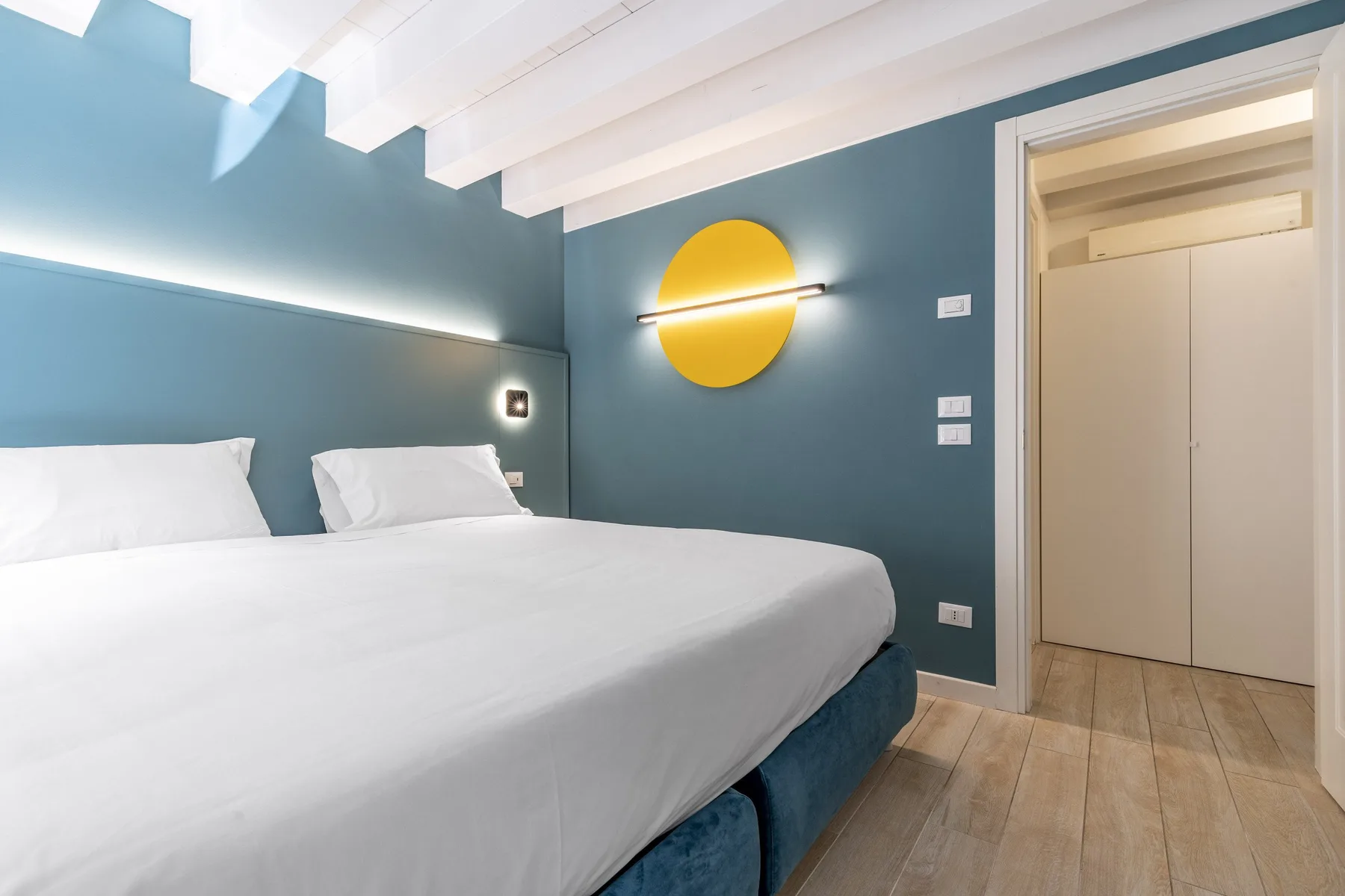 A bedroom with a neatly made bed and a yellow circular wall light.