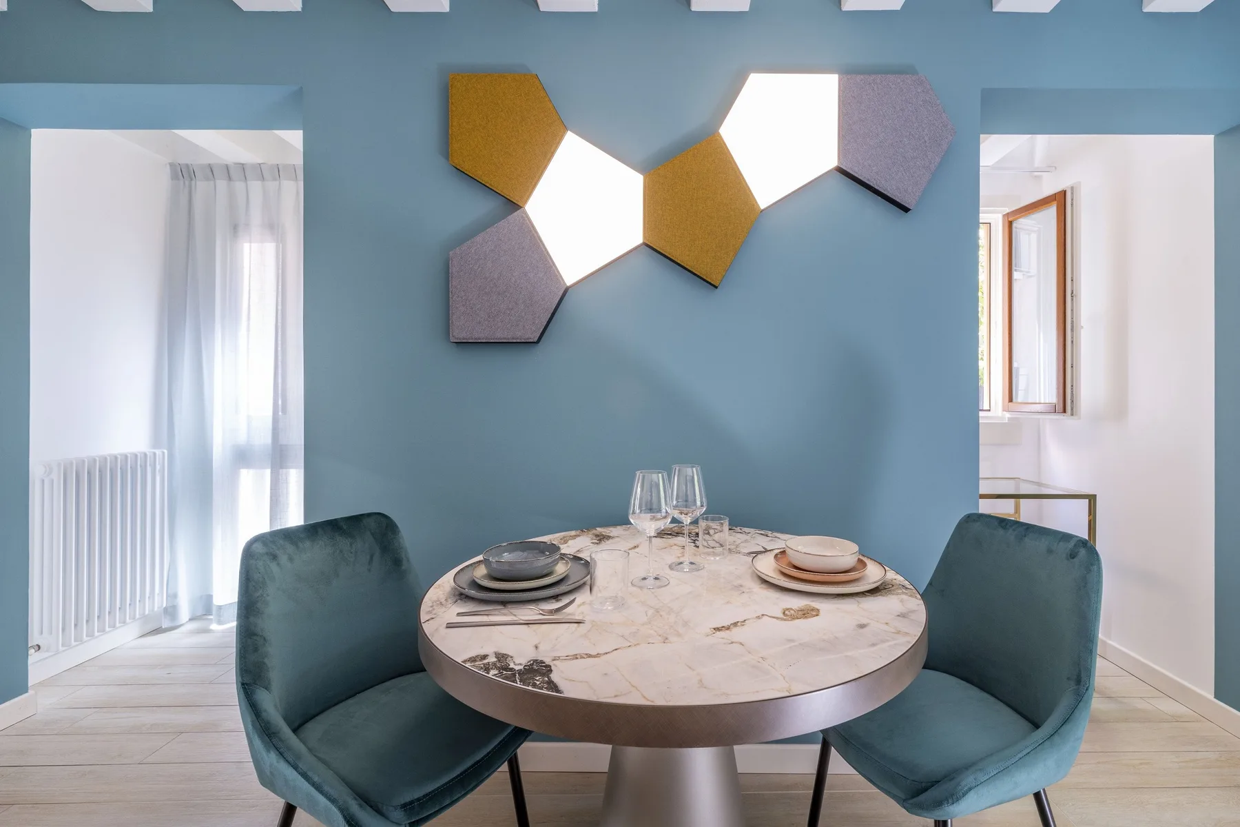 A dining area with a round table and two upholstered seats against a blue wall.