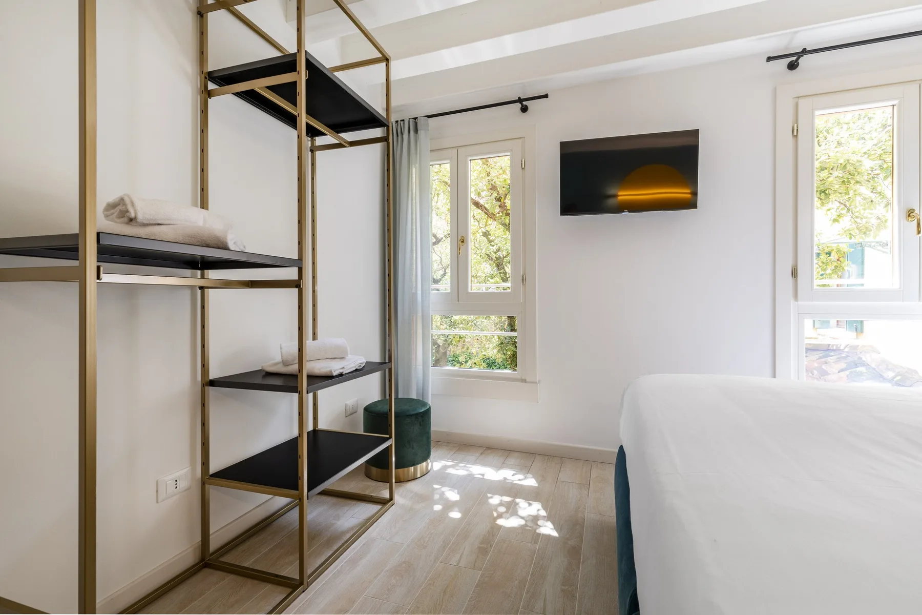 A bright bedroom with a bed, open shelving, and windows.