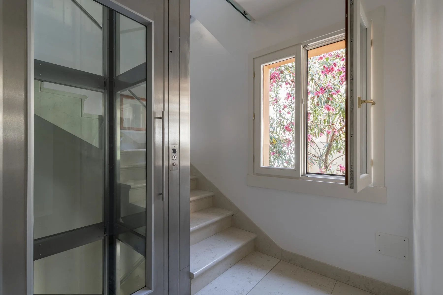 An indoor stairwell with a window overlooking flowering branches.