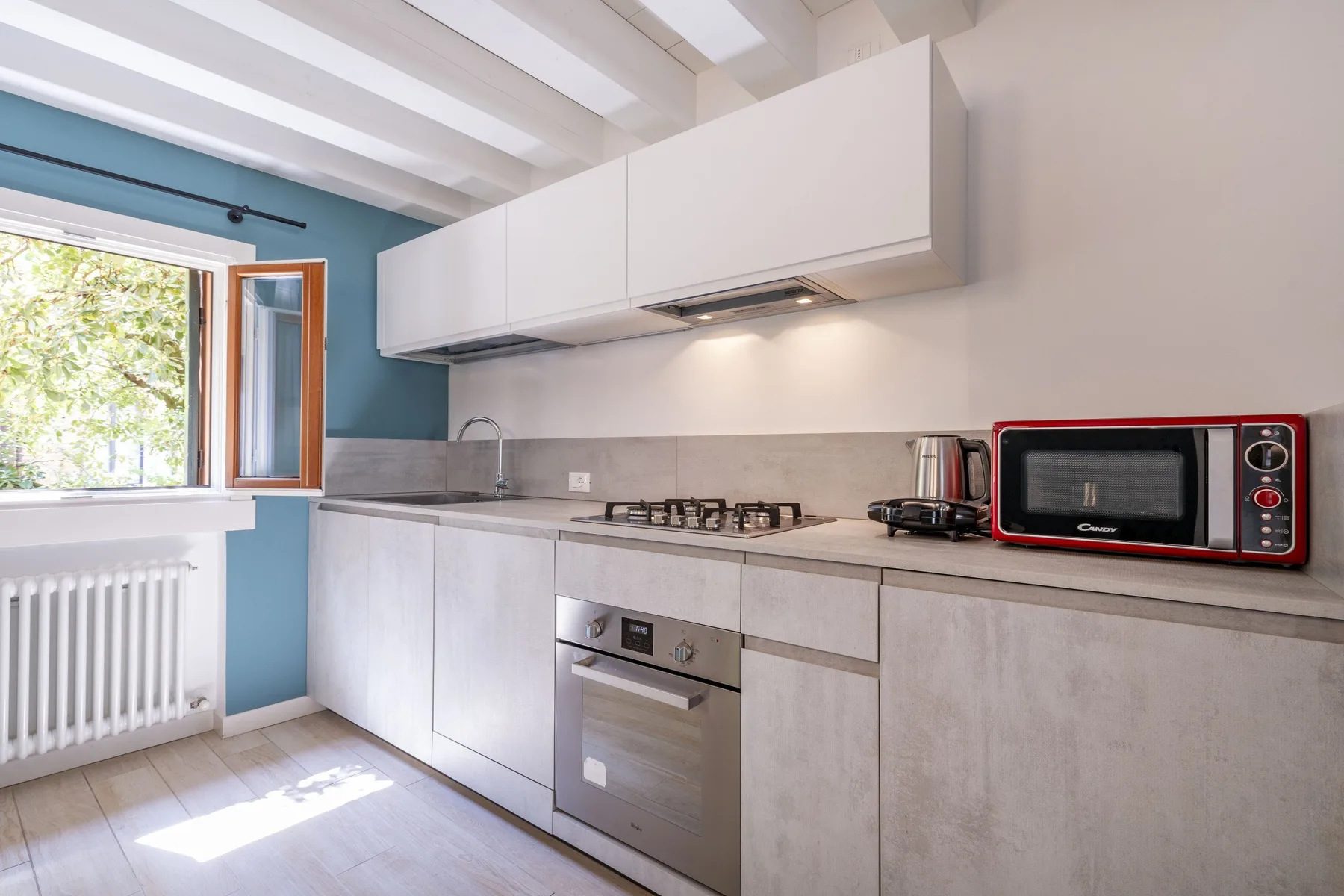 A bright modern kitchen with white cabinets, a countertop, and a red microwave.