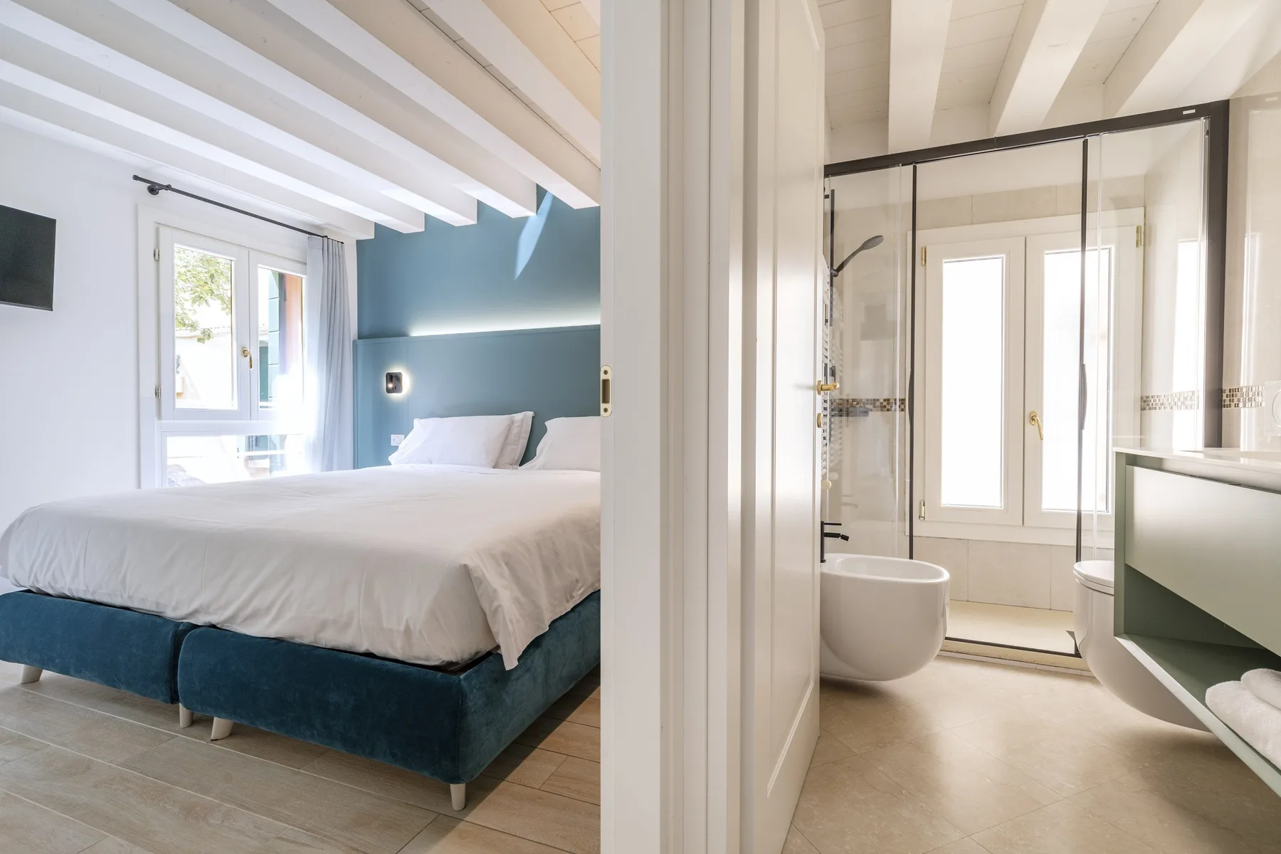 A bedroom with a bed and an adjoining bathroom with a glass shower.