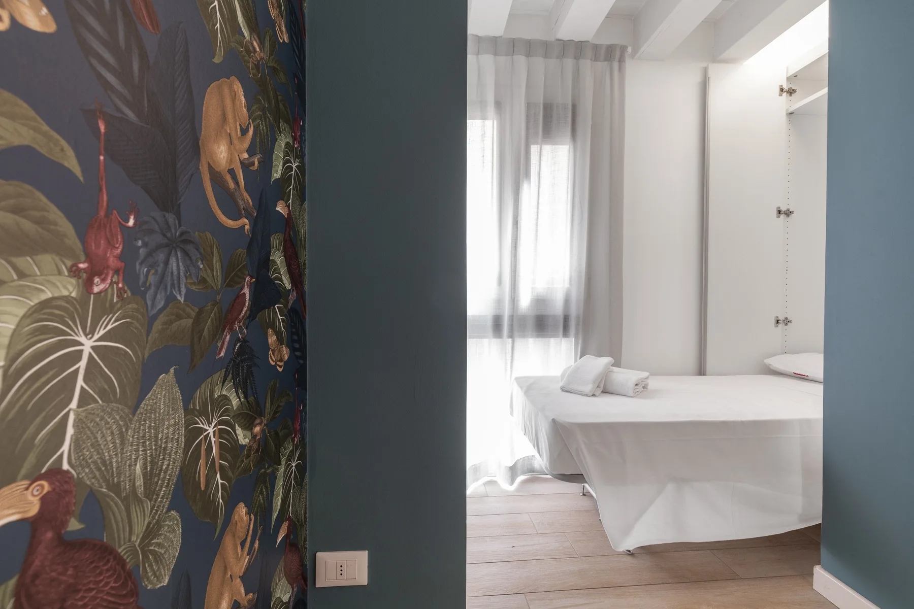 A bright bedroom with a bed beside a tall curtained window.