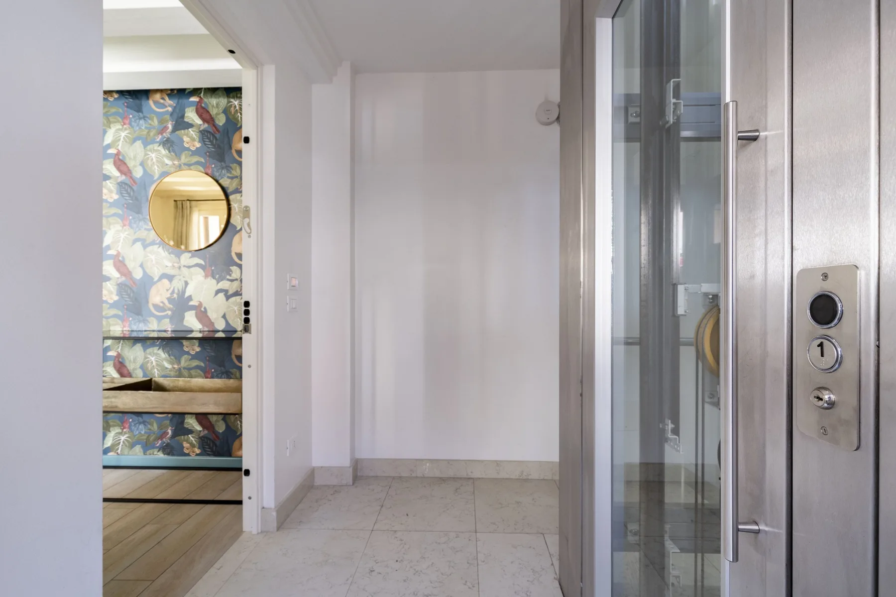 An elevator opens onto a hallway beside a room with colorful floral wallpaper.