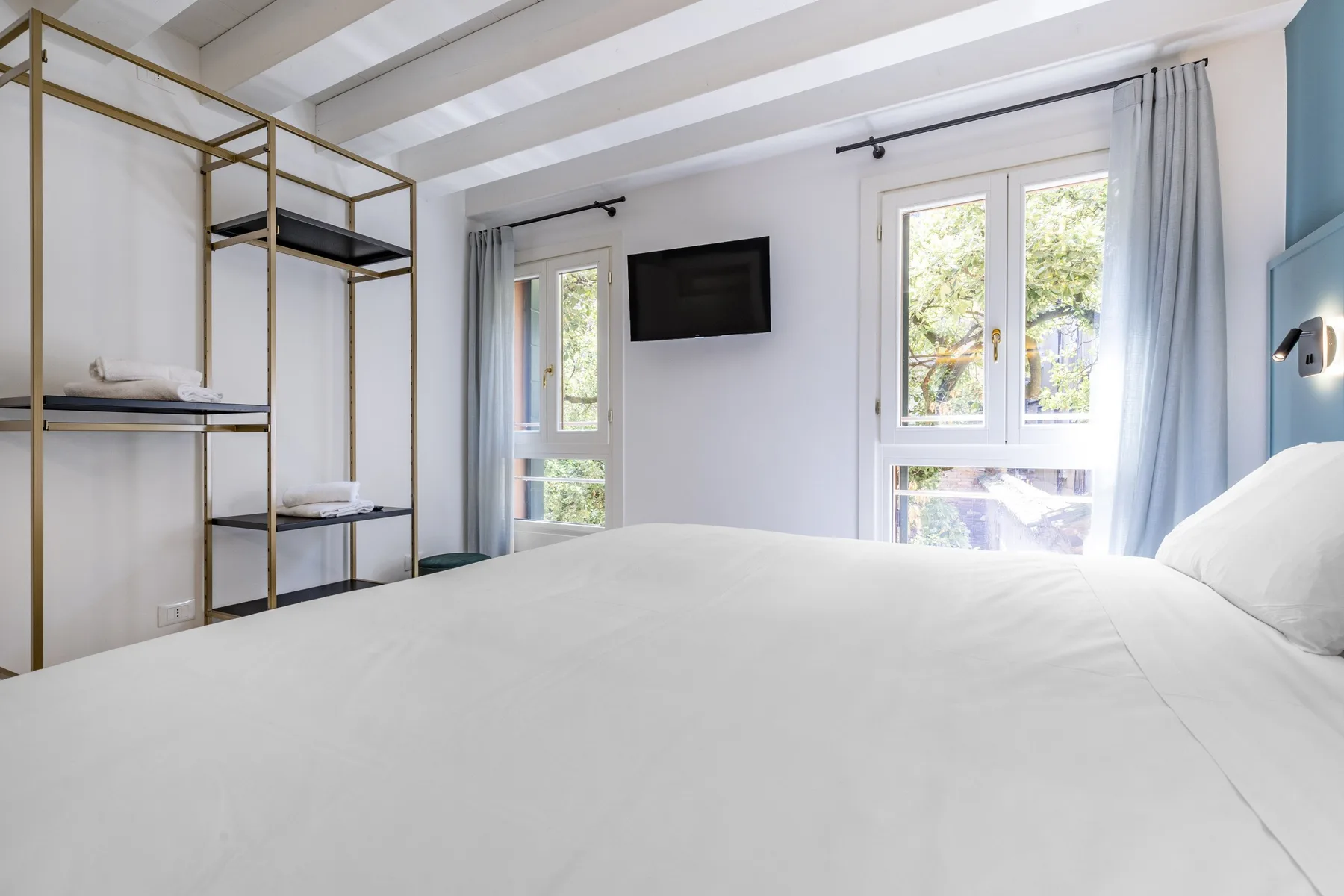 A bright bedroom with a white bed, large windows, and a wall-mounted television.
