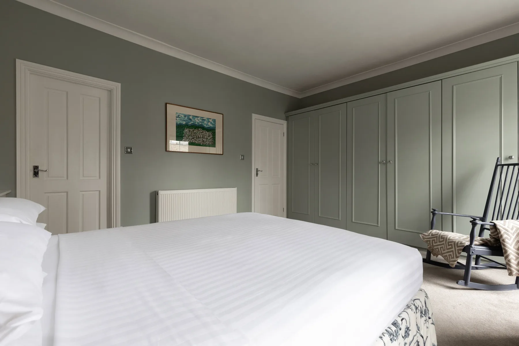 A bedroom with a bed, built-in wardrobes, and a rocking chair.