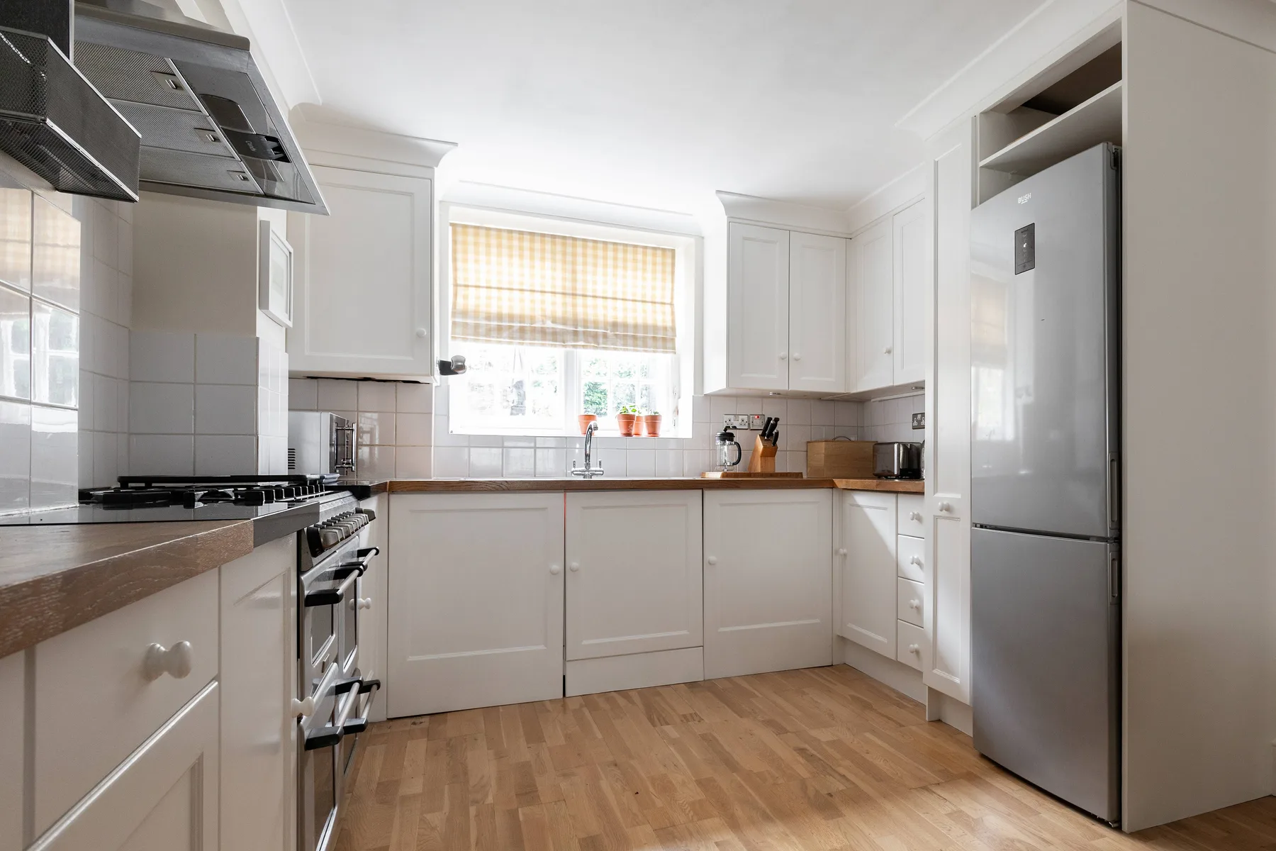 A bright kitchen with white cabinetry, a central window, and wood flooring.