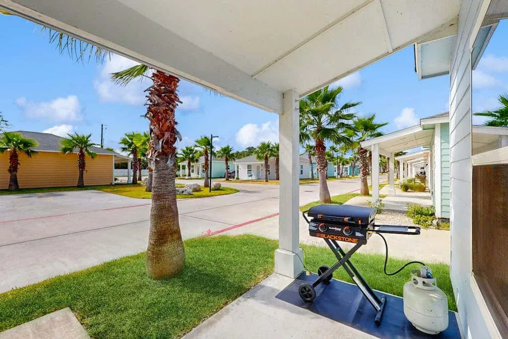 Un patio cubierto da a un patio residencial con palmeras y una parrilla junto a la zona de estar.