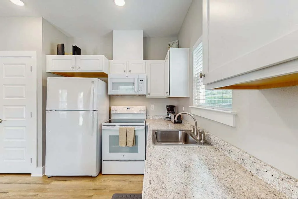 Una cocina luminosa con gabinetes blancos, electrodomésticos y una encimera larga.