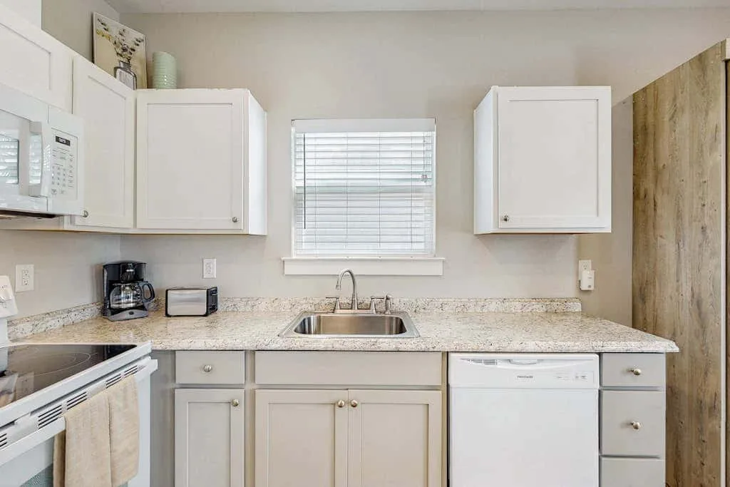 Una cocina luminosa con gabinetes blancos, un fregadero y una ventana con persianas.