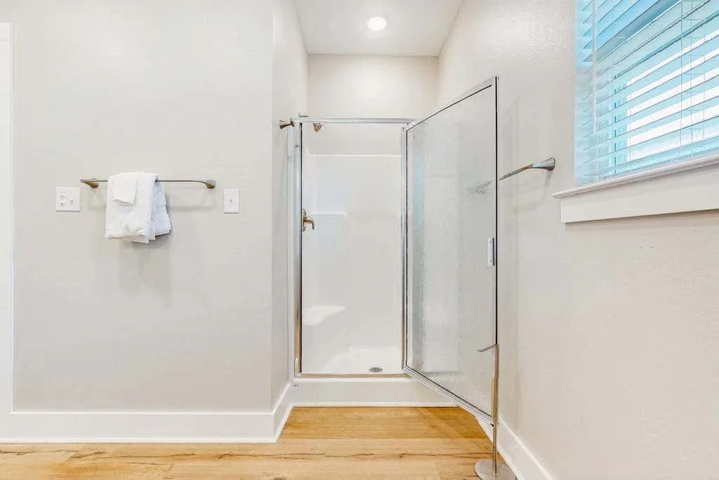 Un baño luminoso con una ducha de vidrio y una ventana con persianas.