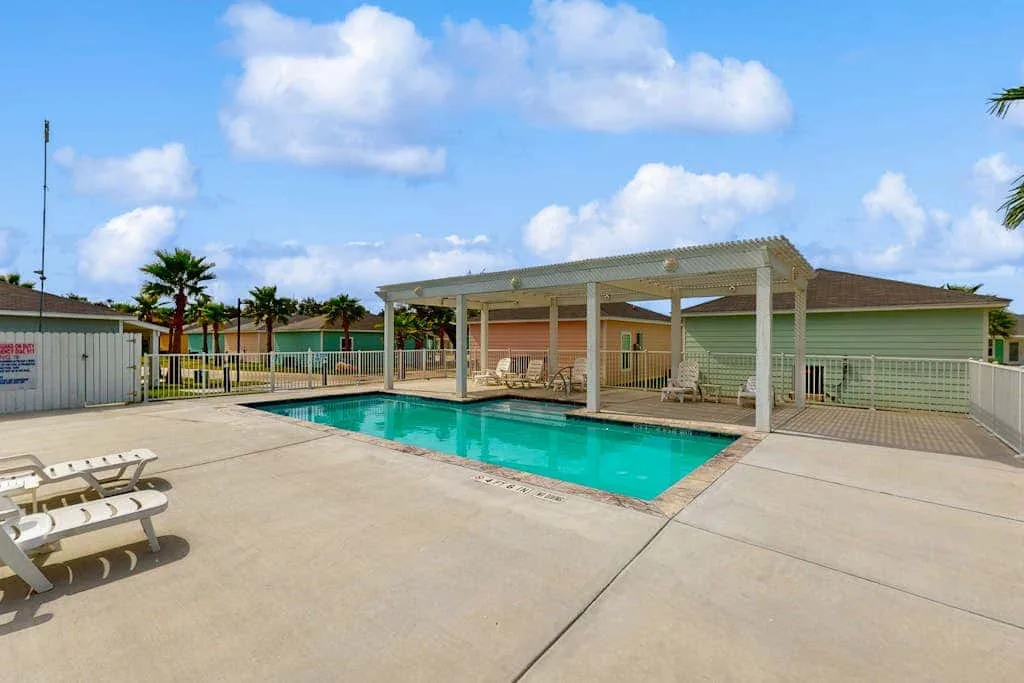 Una piscina al aire libre junto a una zona de estar cubierta y una terraza pavimentada.